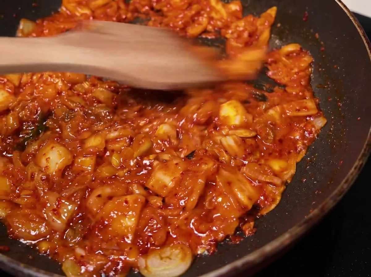Mieszanka kimchi smażona na patelni drewnianą łopatką.