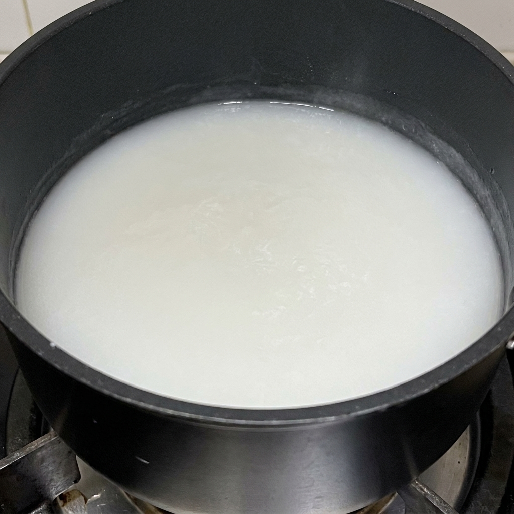 Gęsta, biała pasta z mąki ryżowej gotująca się w czarnym garnku.