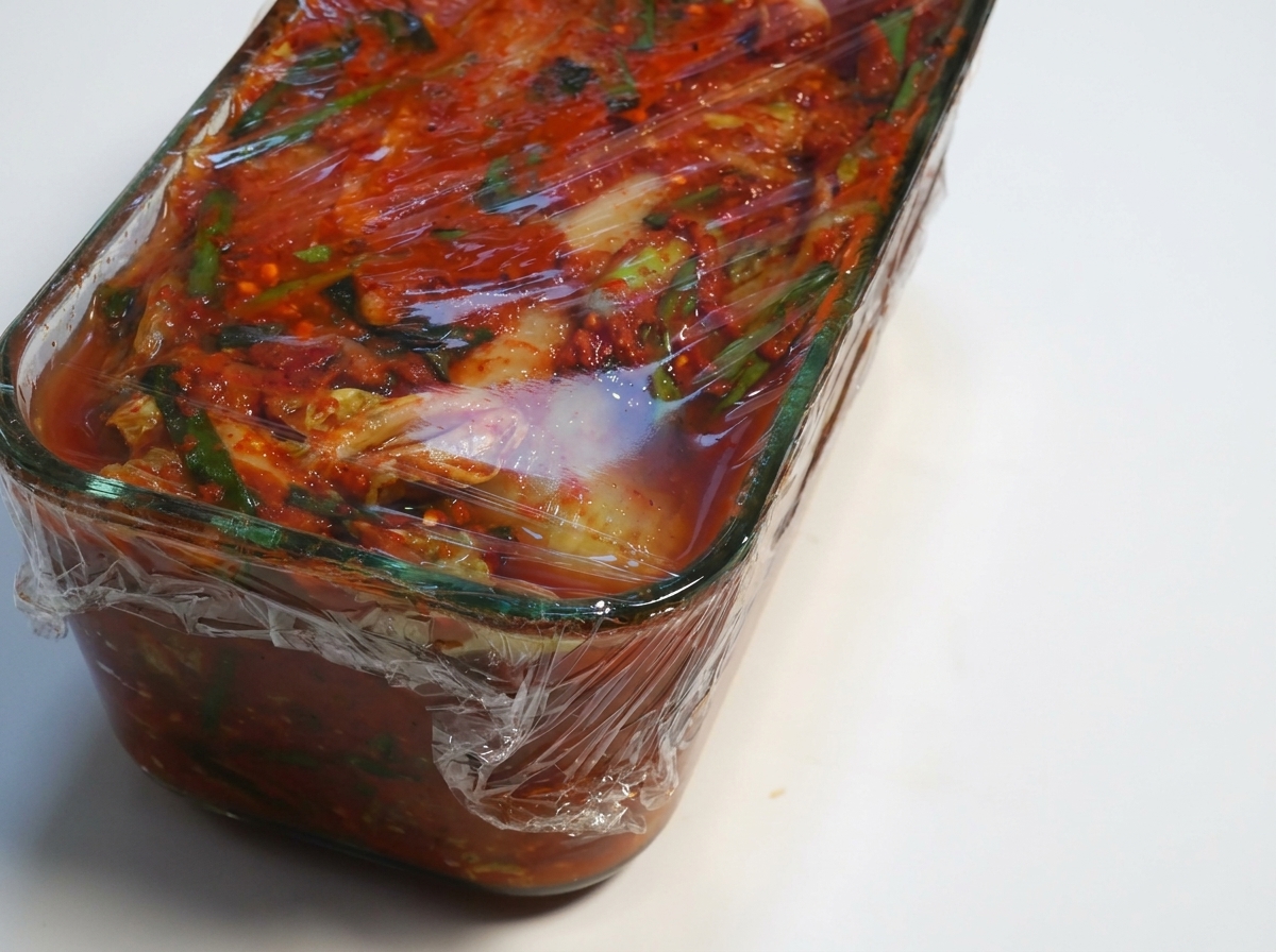 Pojemnik ze sfermentowanym kimchi z odwijaną folią spożywczą.
