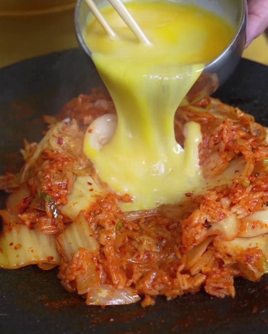 Roztrzepane jajka wlewane na kopczyk smażonego ryżu z kimchi na gorącej patelni.