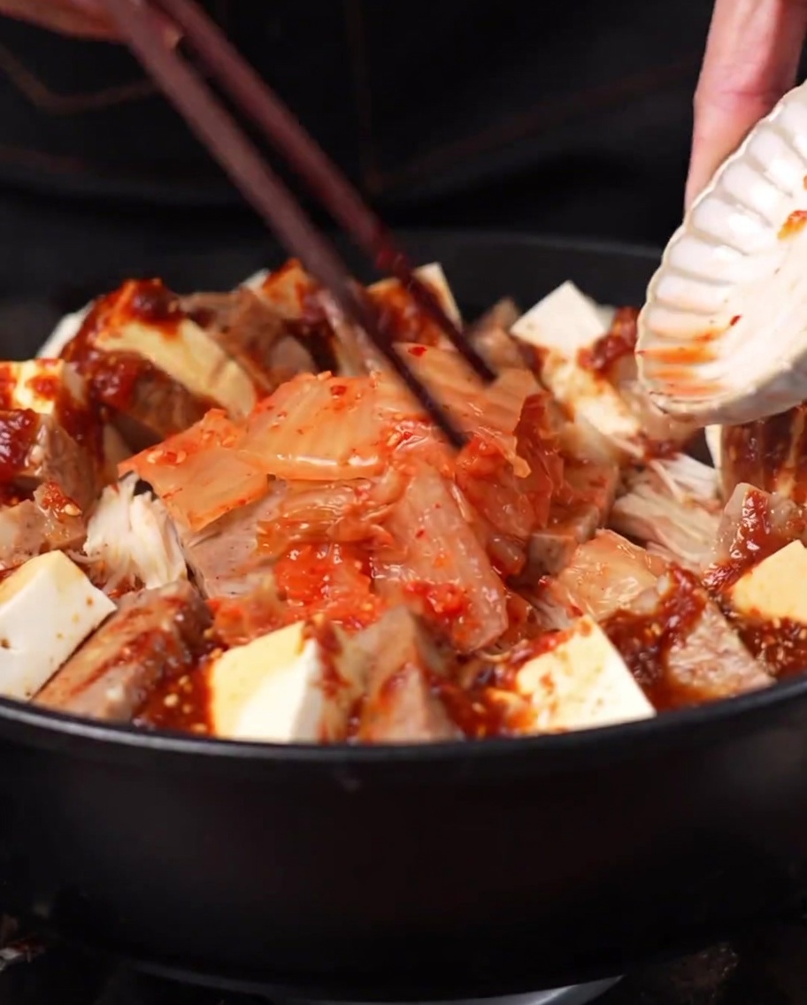Kopiec kimchi dodawany na środek garnka otoczony innymi składnikami.