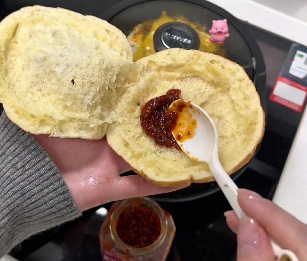 Łyżka czerwonego sosu chili rozsmarowywana na miękkiej, wewnętrznej stronie otwartej bułki.