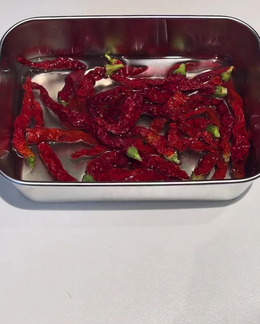 Suszone skórki czerwonego chili moczące się w metalowym pojemniku wypełnionym gorącą wodą.