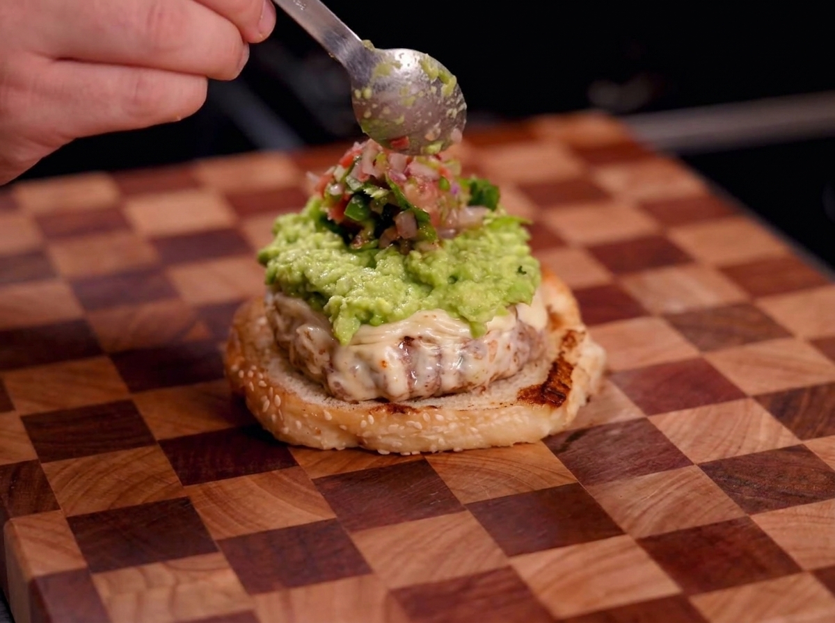 Dłoń z łyżką nakładającą czerwoną salsę na guacamole.