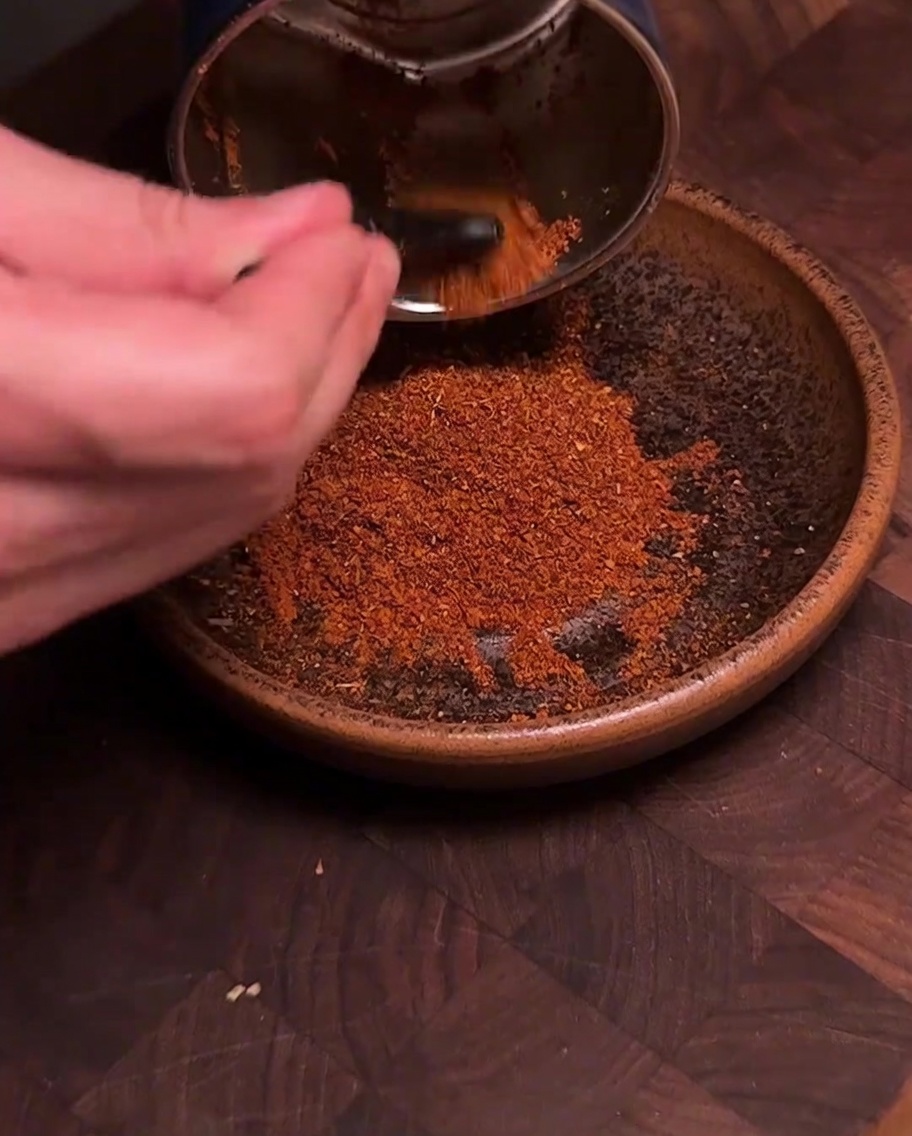 Młynek do przypraw wsypujący świeżo zmielony, intensywnie czerwony proszek chili z przyprawami do brązowej ceramicznej miski.