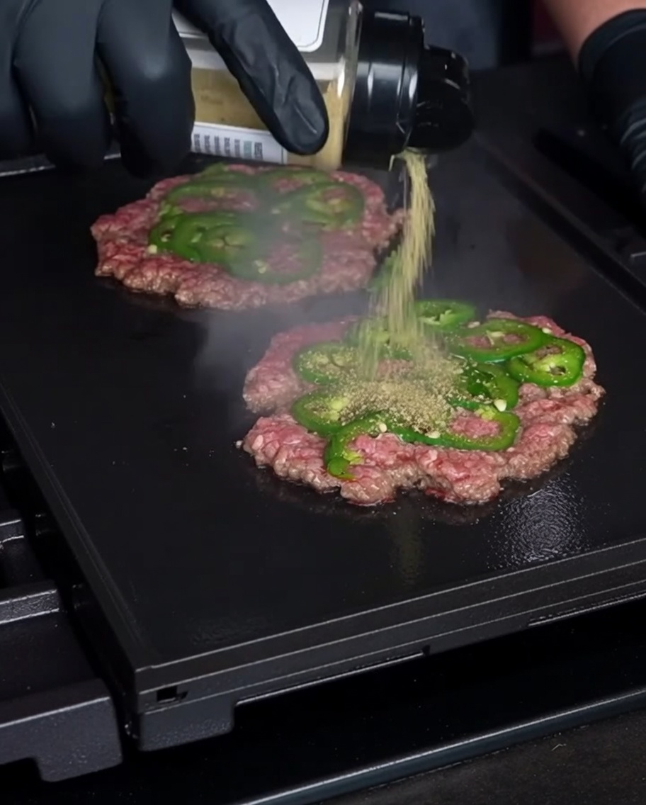 Posypywanie przyprawami zmiażdżonych burgerów na grillu.