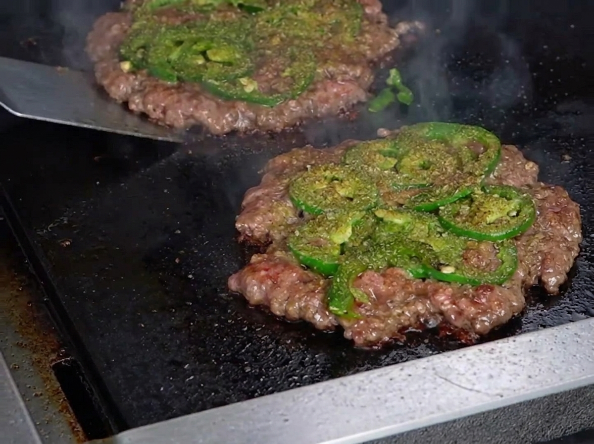 Odwracanie burgera metalową szpatułką z widoczną karmelizowaną skórką.