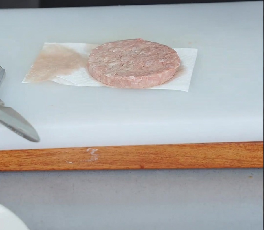 Surowy kotlet wołowy na ręczniku papierowym, z drugim ręcznikiem dociskanym z góry, aby wchłonąć wilgoć.