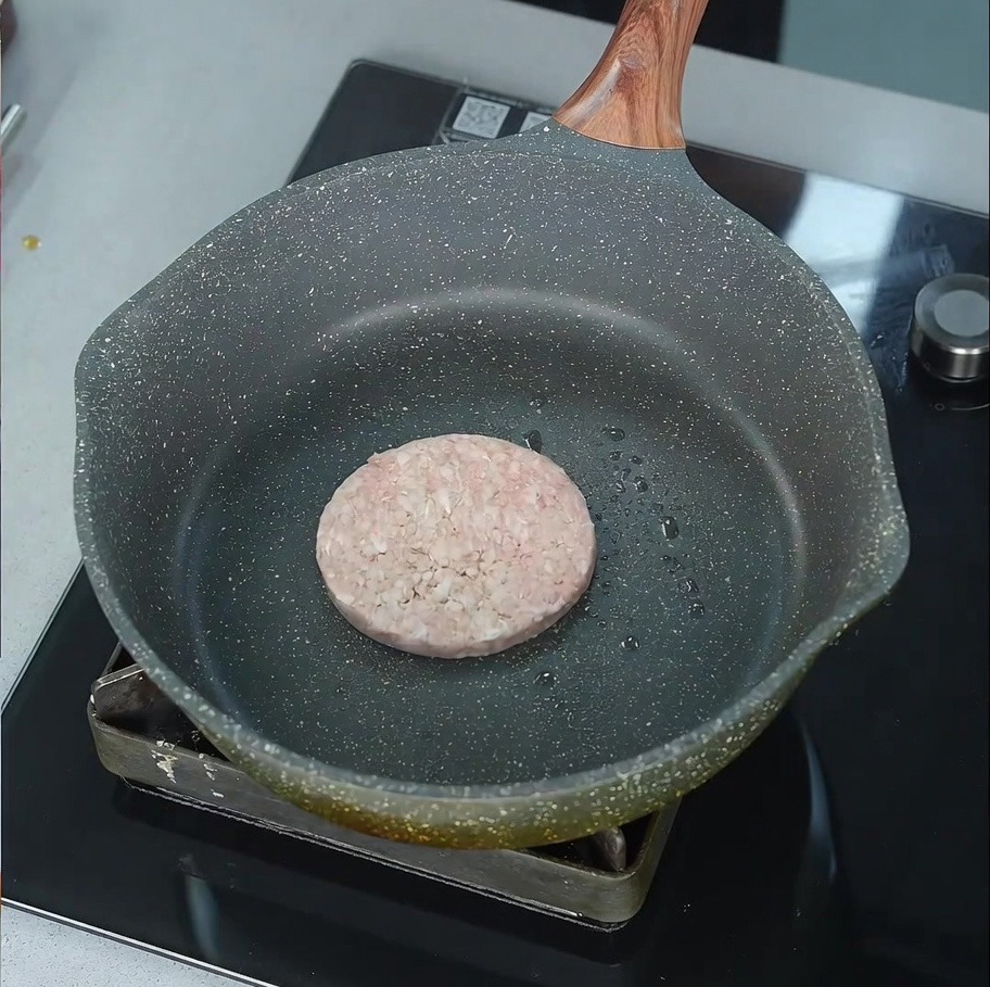 Surowy kotlet wołowy zaczynający skwierczeć na lekko naoliwionej patelni na palniku.