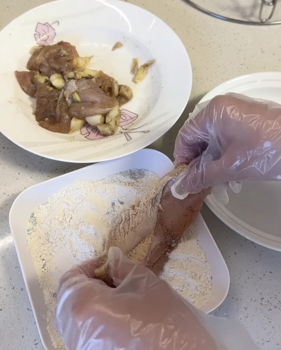 Kawałki kurczaka dociskane do mieszanki panierującej na białym talerzu.