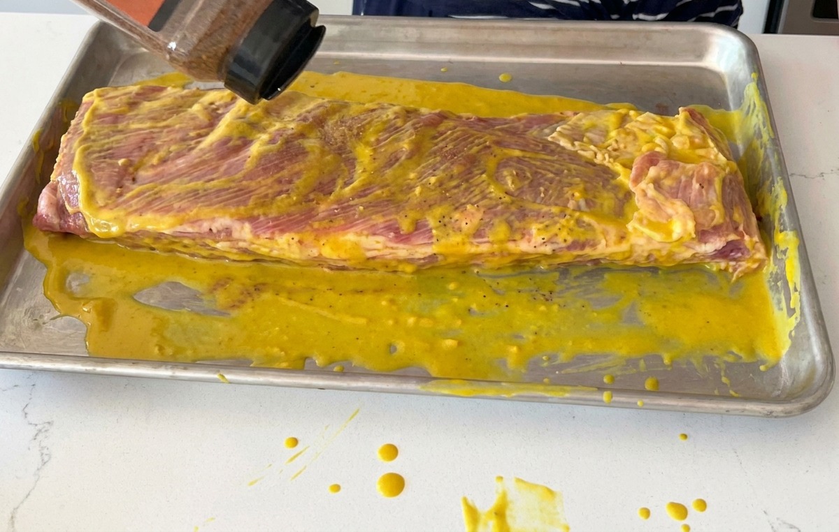 Posypywanie żeber pokrytych musztardą suchą przyprawą BBQ.