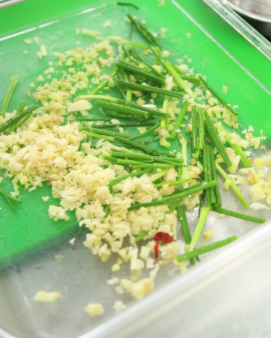 Pojemnik z posiekanym czosnkiem, zielonym szczypiorkiem i czerwoną pastą paprykową gochujang.