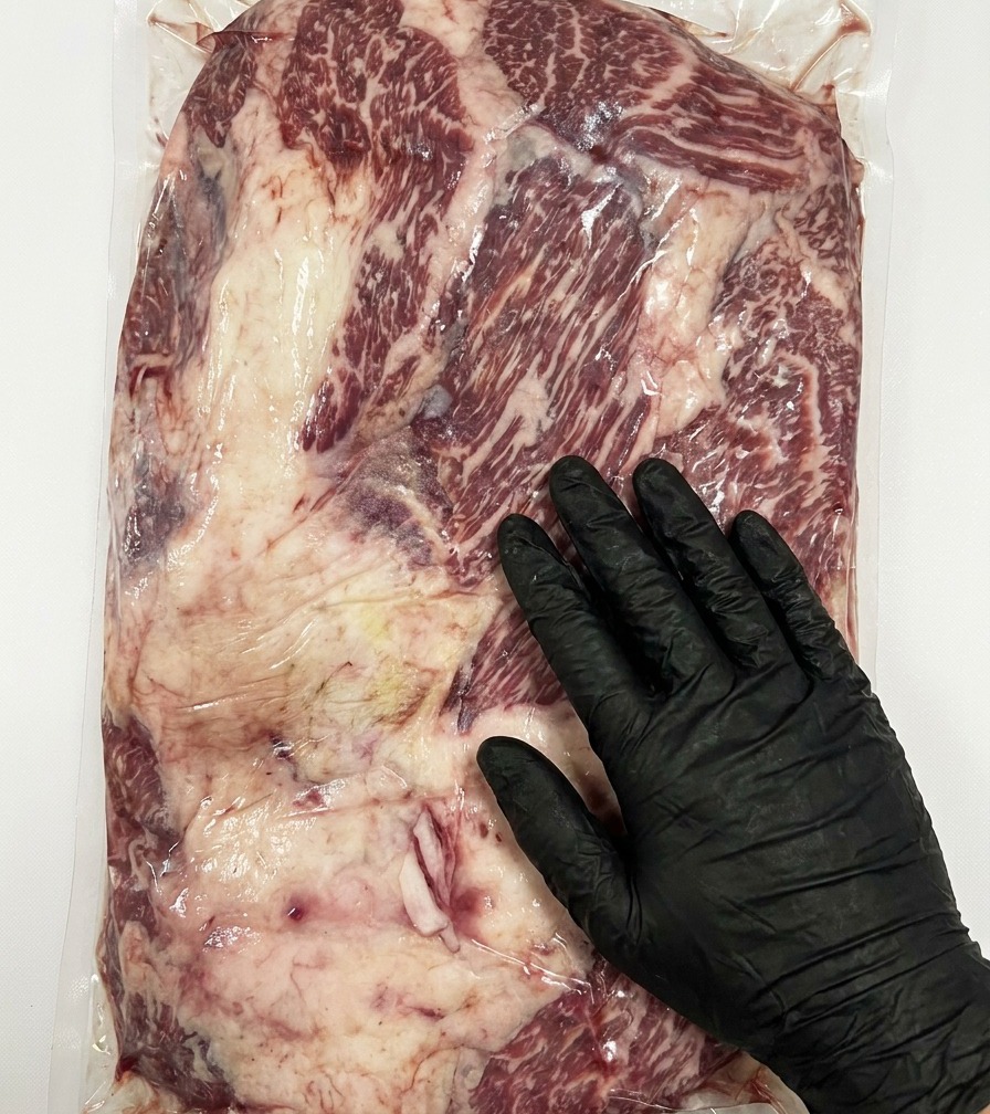 Zbliżenie na nóż usuwający nadmiar tłuszczu z powierzchni surowego mostka Stone Axe Wagyu.