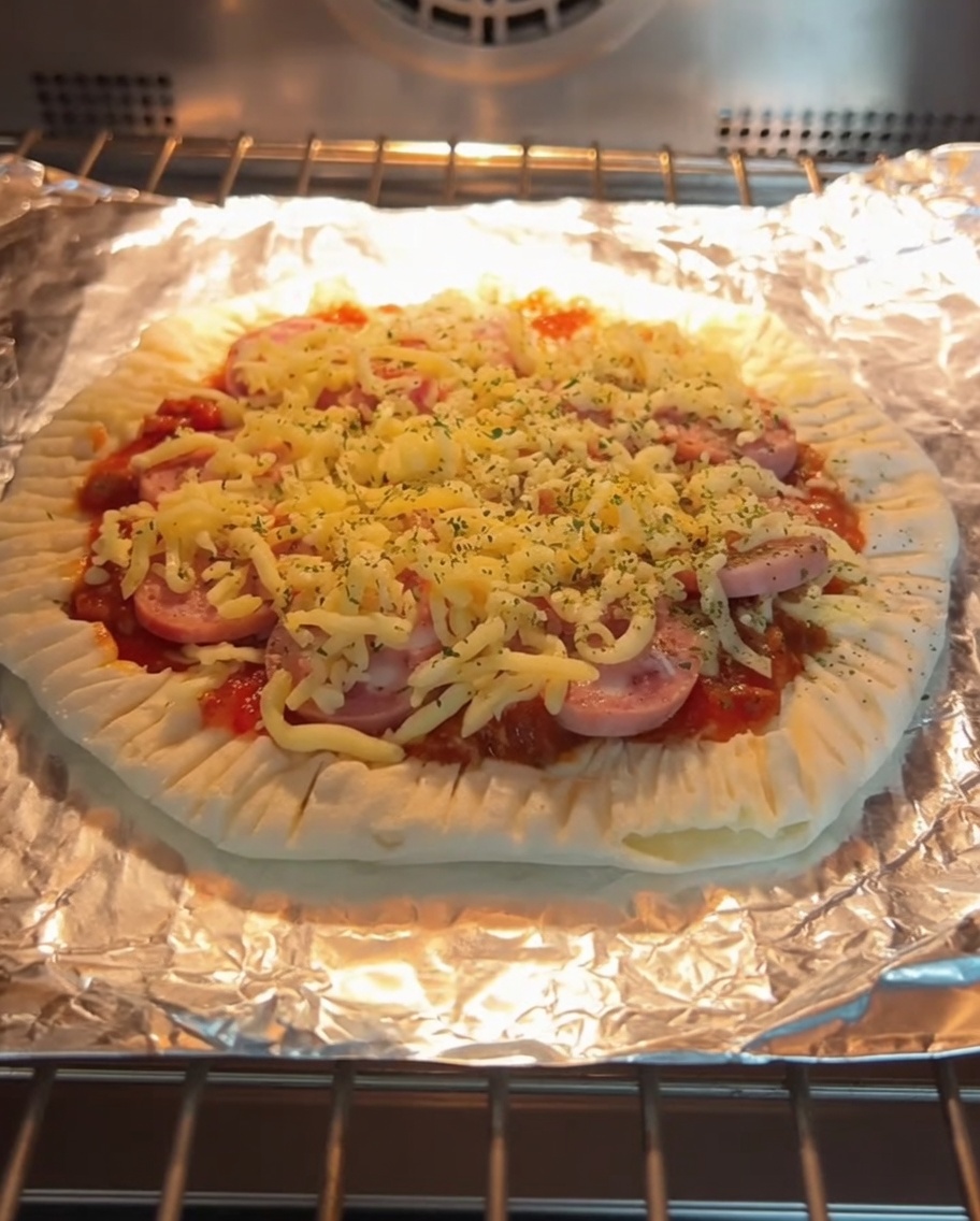 Upieczona pizza na placku szczypiorkowym z roztopionym serem i kiełbasą, znajdująca się w piekarniku na ruszcie.