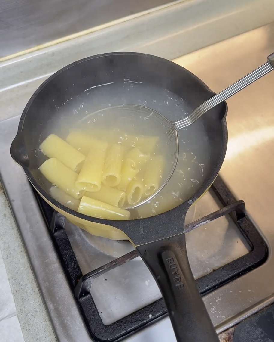Druciane sitko wyjmujące ugotowane rigatoni z wrzątku w czarnym garnku.