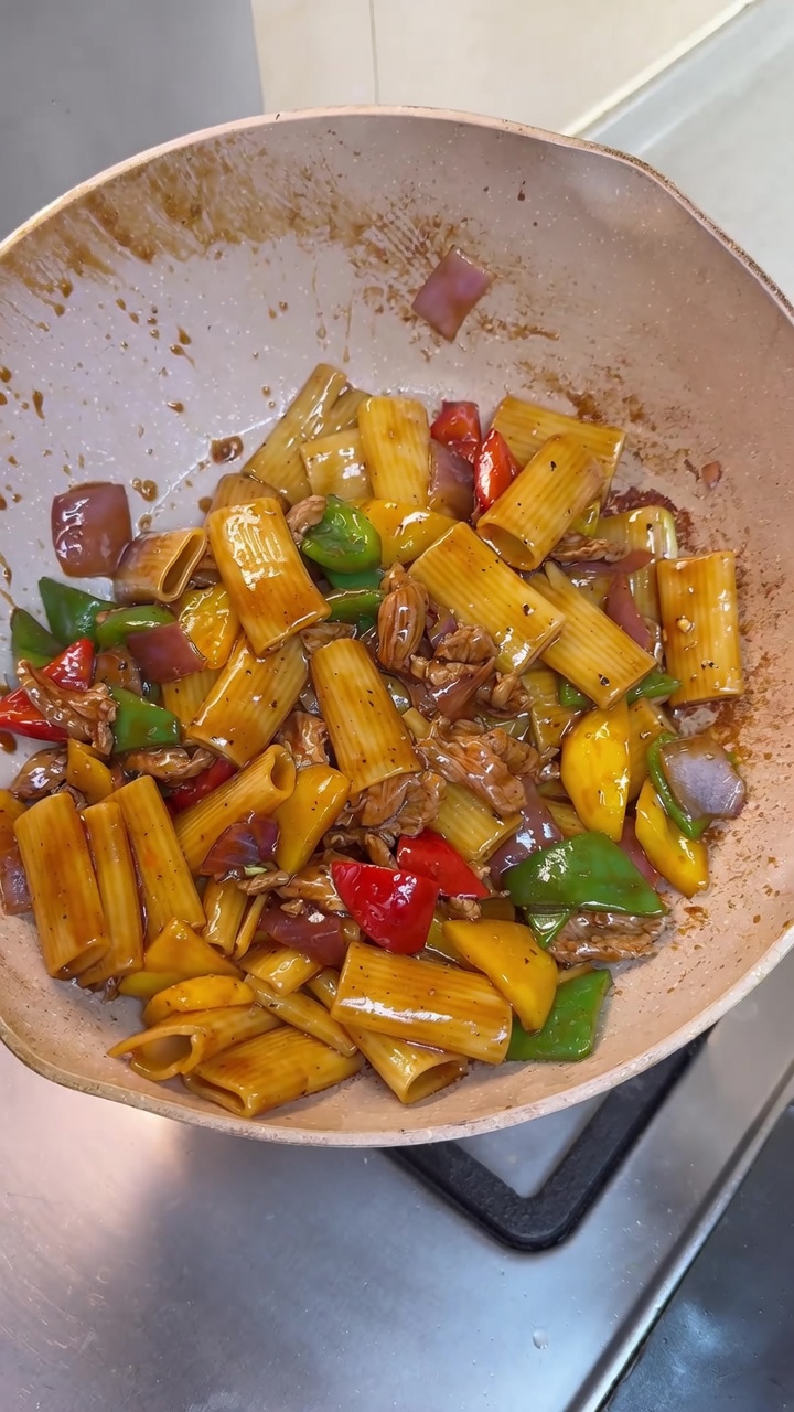 Stir-fried rigatoni w bogatym, lśniącym sosie z soczystą wieprzowiną i kolorowymi kawałkami papryki.