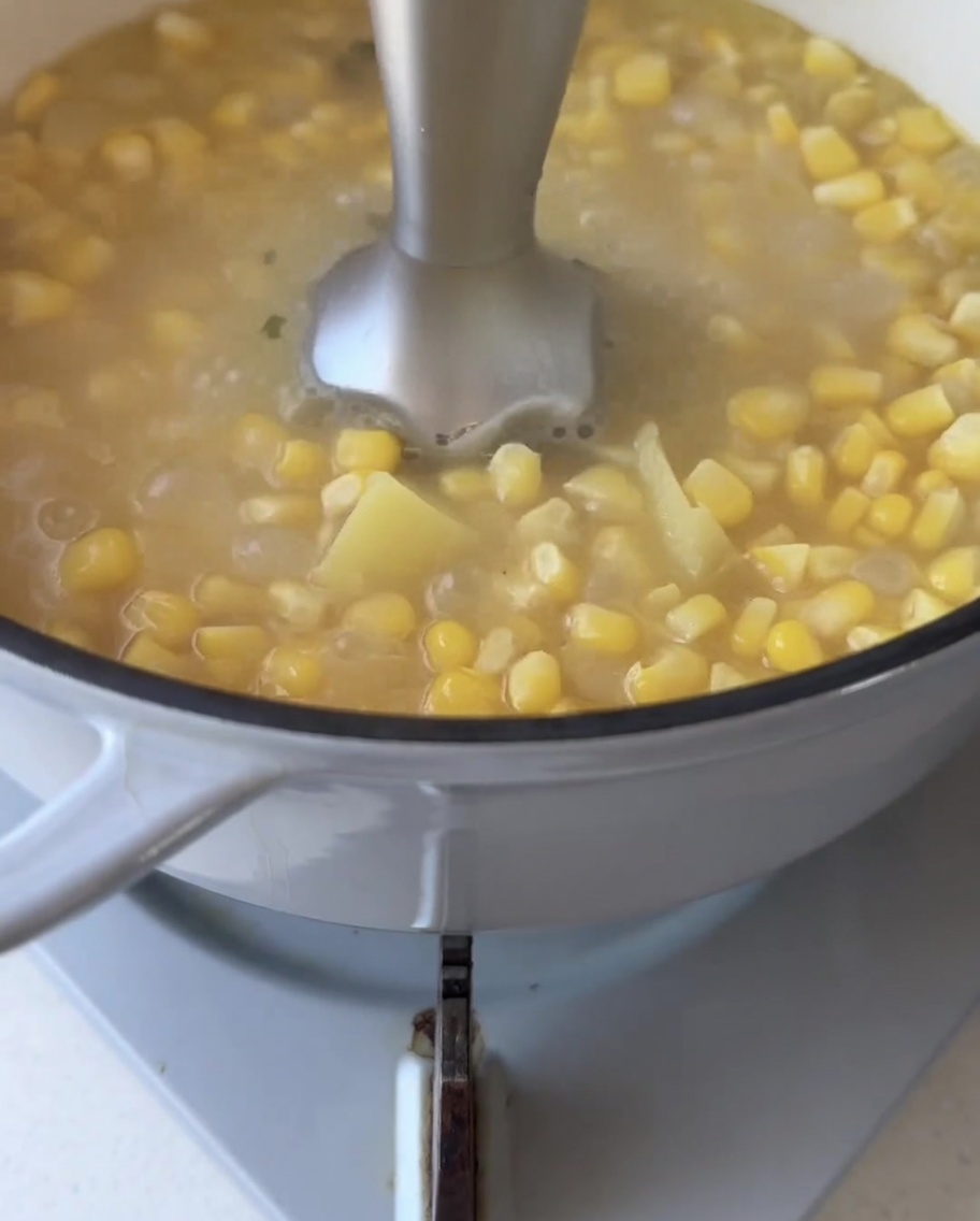 Blender ręczny zanurzony w garnku z zupą, miksujący warzywa na gładką masę.