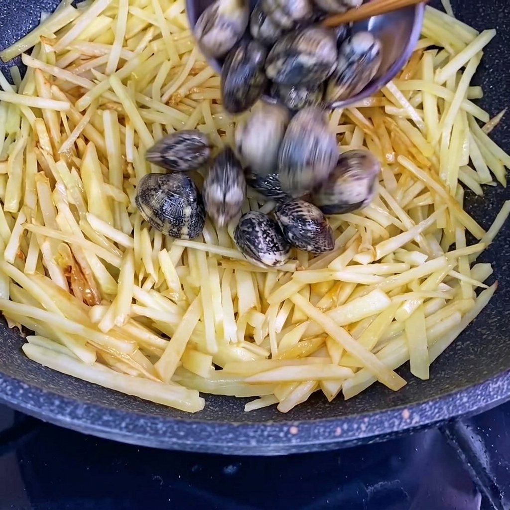 Świeże małże w muszlach dodawane do woka z przyprawionymi ziemniakami.