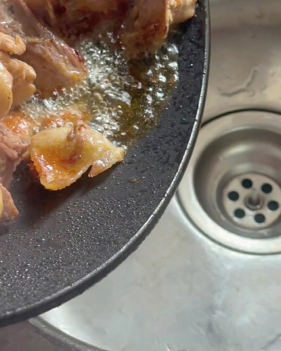 Przechylony wok z wytopionym tłuszczem z kurczaka wylewanym do zlewu.