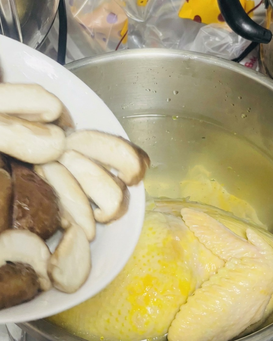 Pokrojone grzyby shiitake wsypywane z talerza do garnka z kurą.