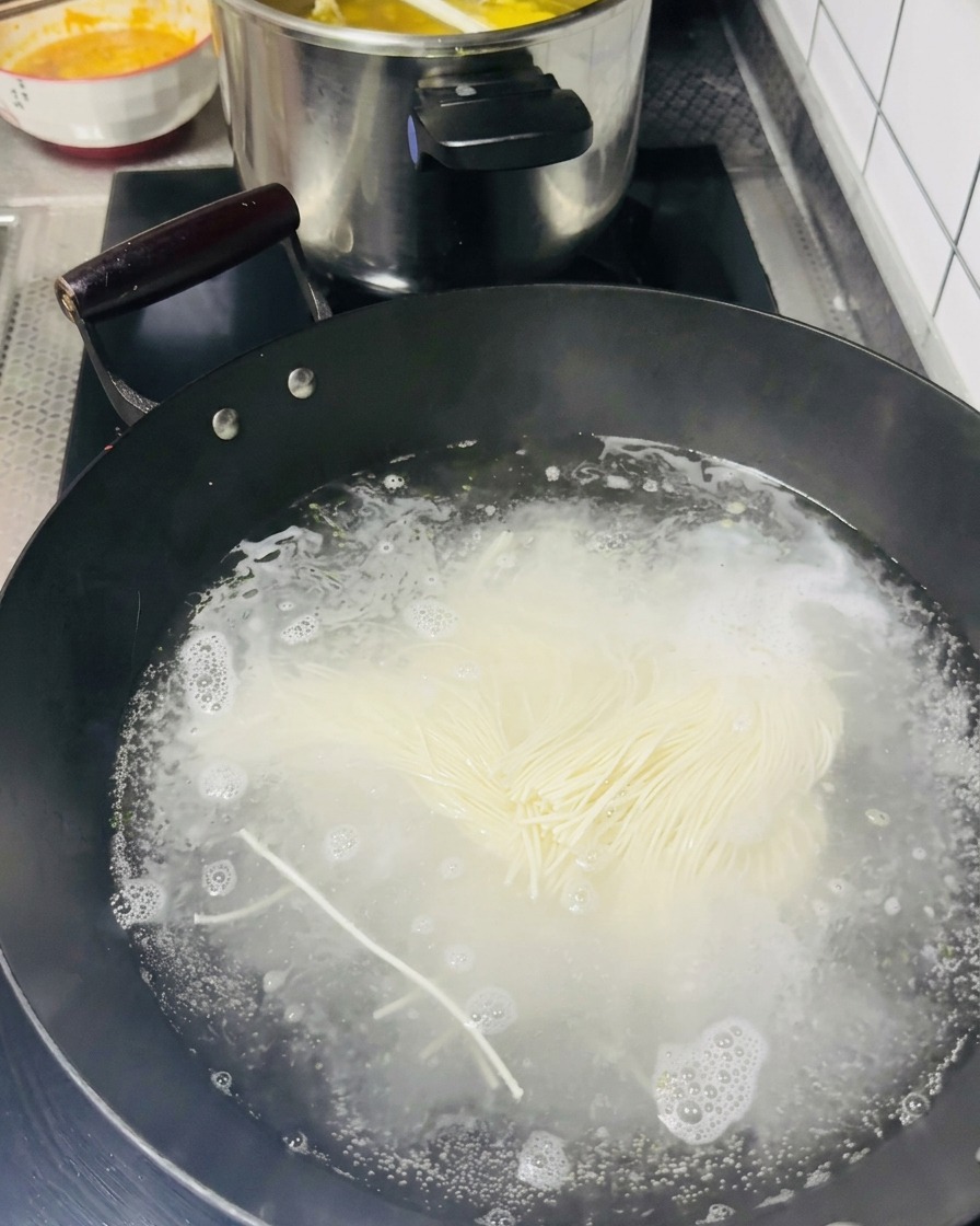 Pęczek cienkiego makaronu wrzucany do wrzącej wody w woku.