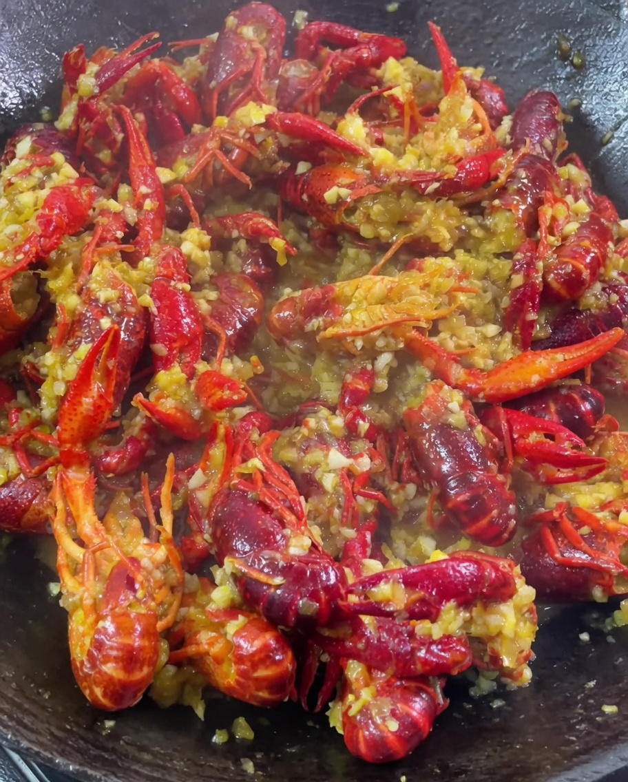 Posiekany czosnek, przyprawa curry i inne dodatki wsypywane do woka z duszącymi się rakami.