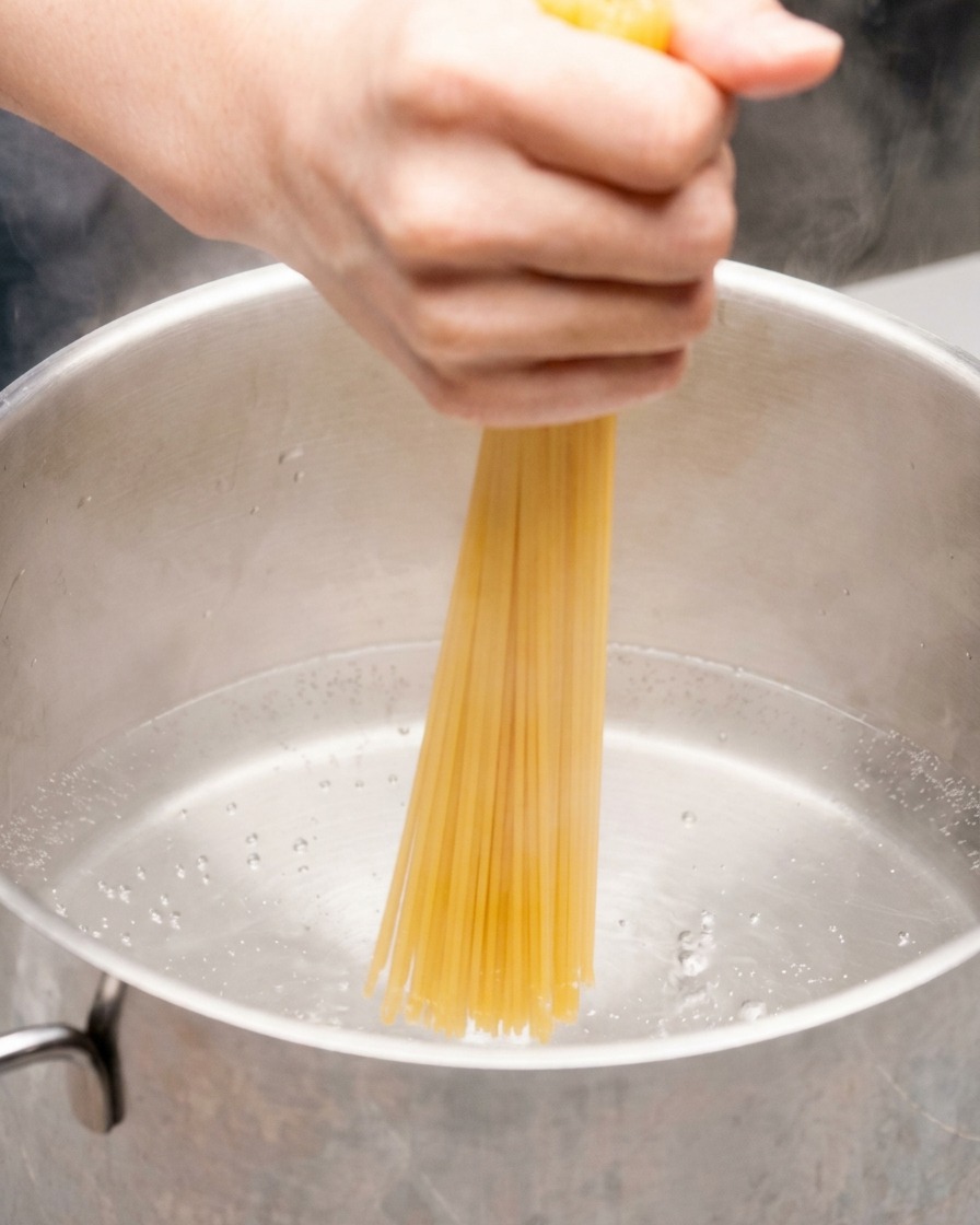 Dłoń popychająca pęczek suchego makaronu spaghetti do garnka z wrzącą wodą.