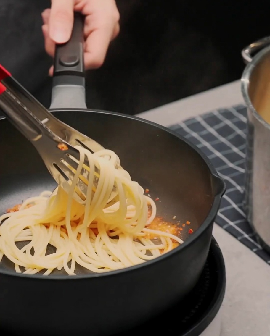Ugotowane spaghetti mieszane szczypcami na patelni z aromatyczną oliwą czosnkową.