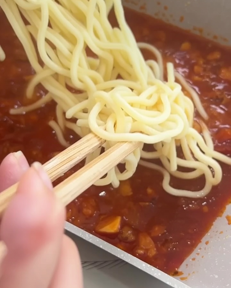 Ugotowany makaron spaghetti mieszany pałeczkami z sosem mięsno-pomidorowym na patelni.