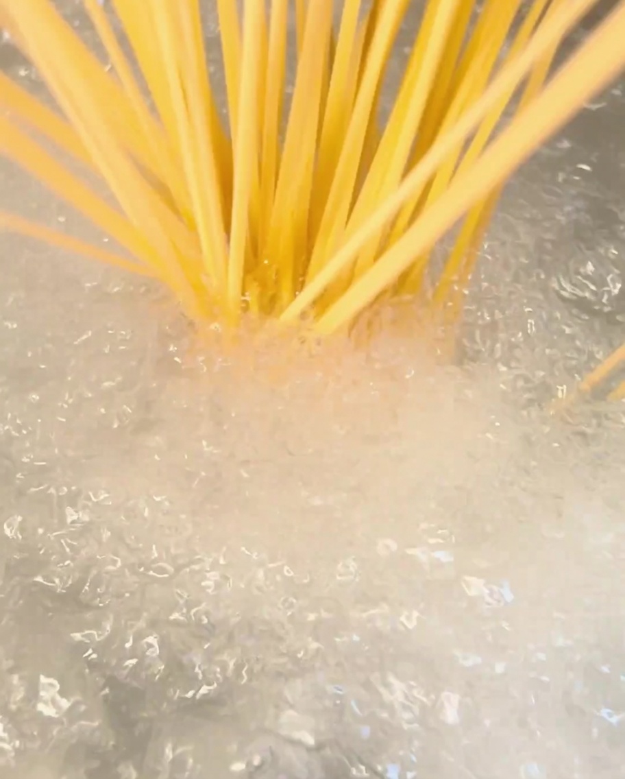 Pęczek suchego spaghetti wkładany do garnka z wrzącą wodą.