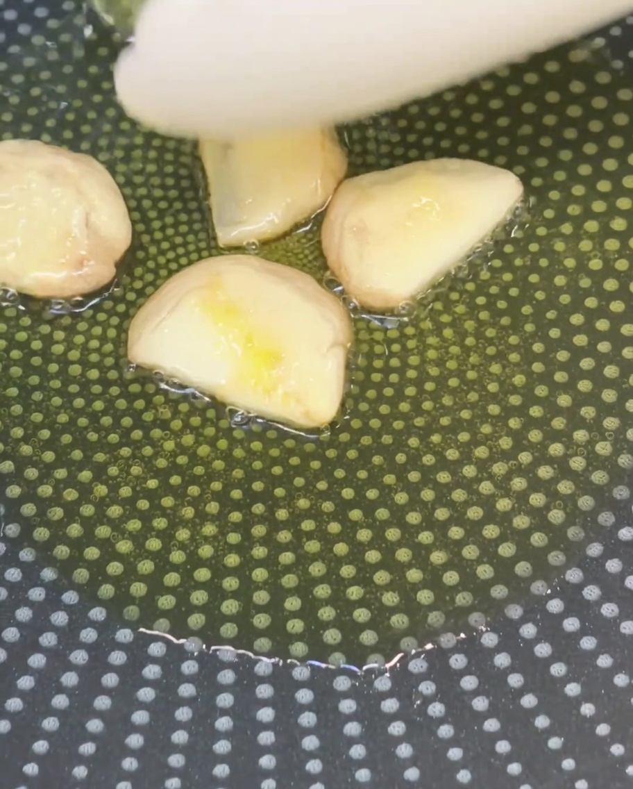 Zmiażdżone ząbki czosnku smażące się na oliwie na patelni.