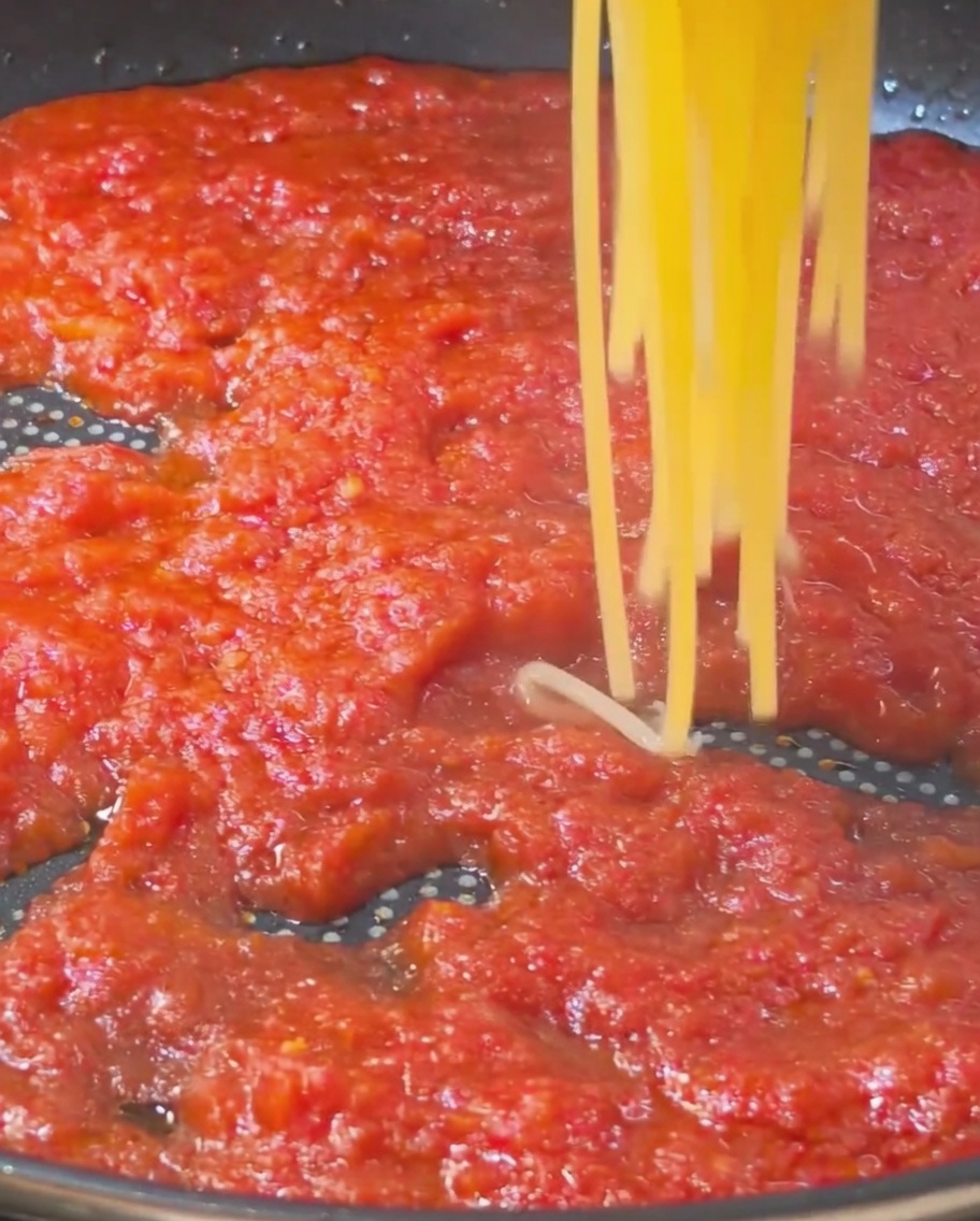 Ugotowane gorące spaghetti przekładane do patelni z gęstym, czerwonym sosem pomidorowym.