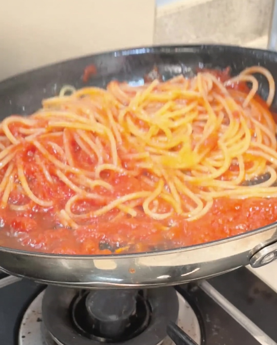 Spaghetti mieszane szczypcami na patelni, w pełni pokryte żywym czerwonym sosem pomidorowym.