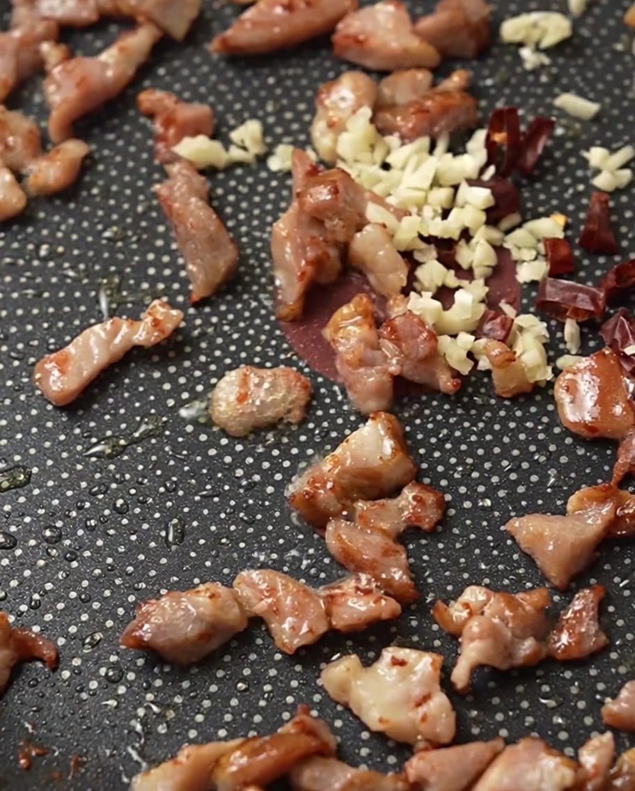 Skwierczący boczek, posiekany czosnek i suszone chili na patelni.