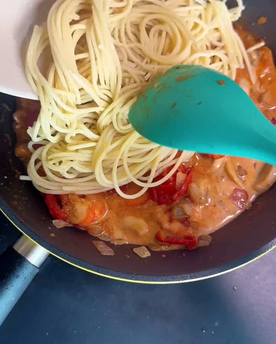 Spaghetti mieszane na patelni z kremowym sosem przy użyciu zielonej łopatki.