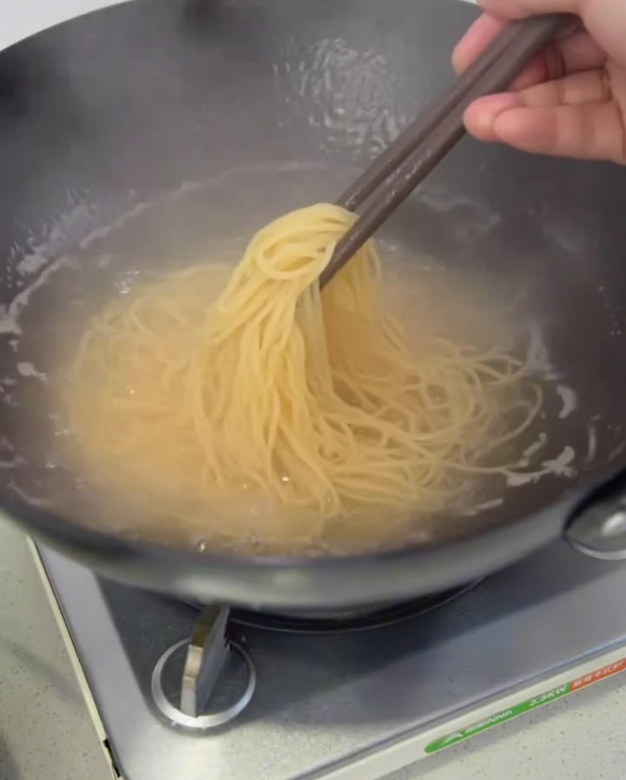 Ugotowany makaron spaghetti wyciągany z garnka za pomocą szczypiec.