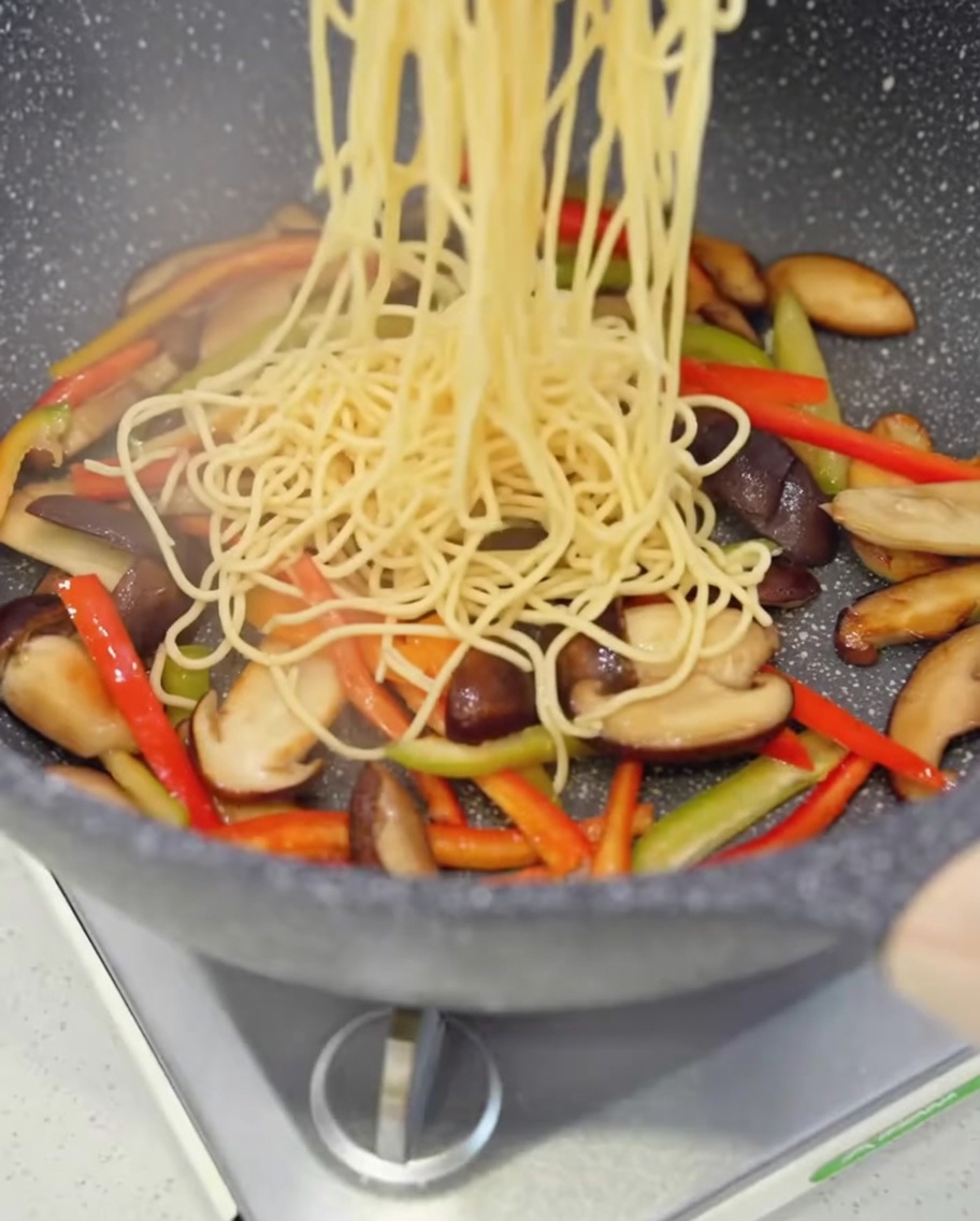 Ugotowane nici spaghetti wrzucane na patelnię z grzybami i papryką.