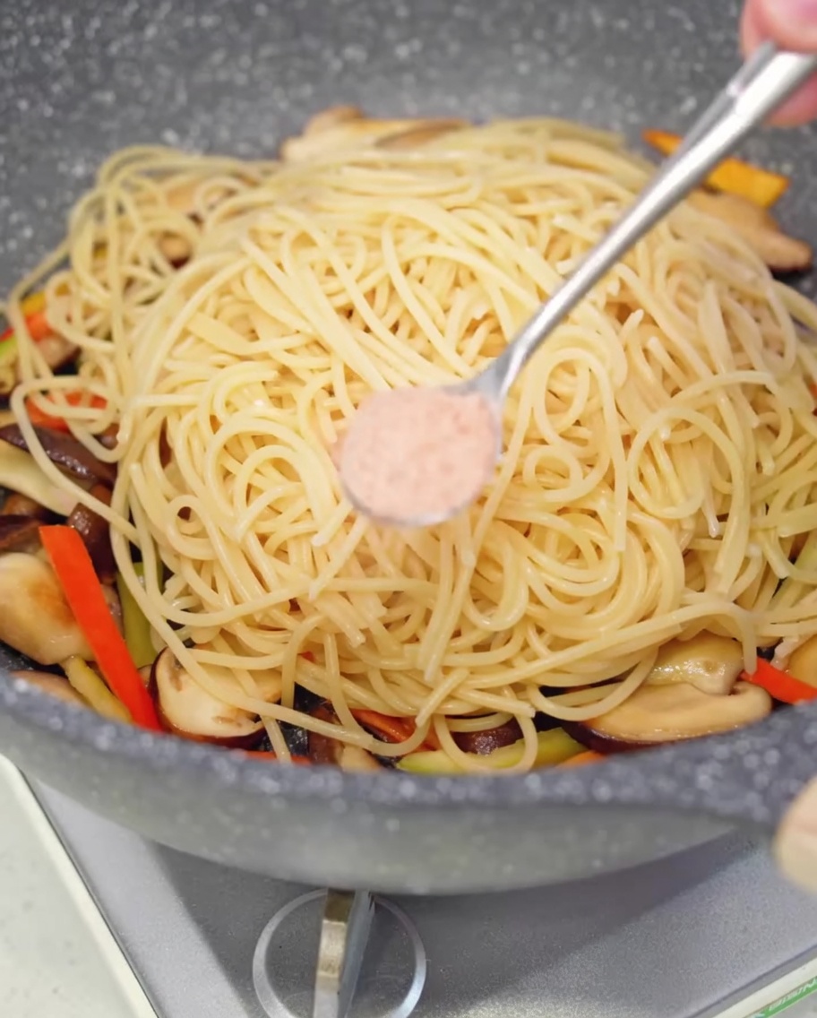 Niewielka porcja różowej soli oprószana na spaghetti na patelni.