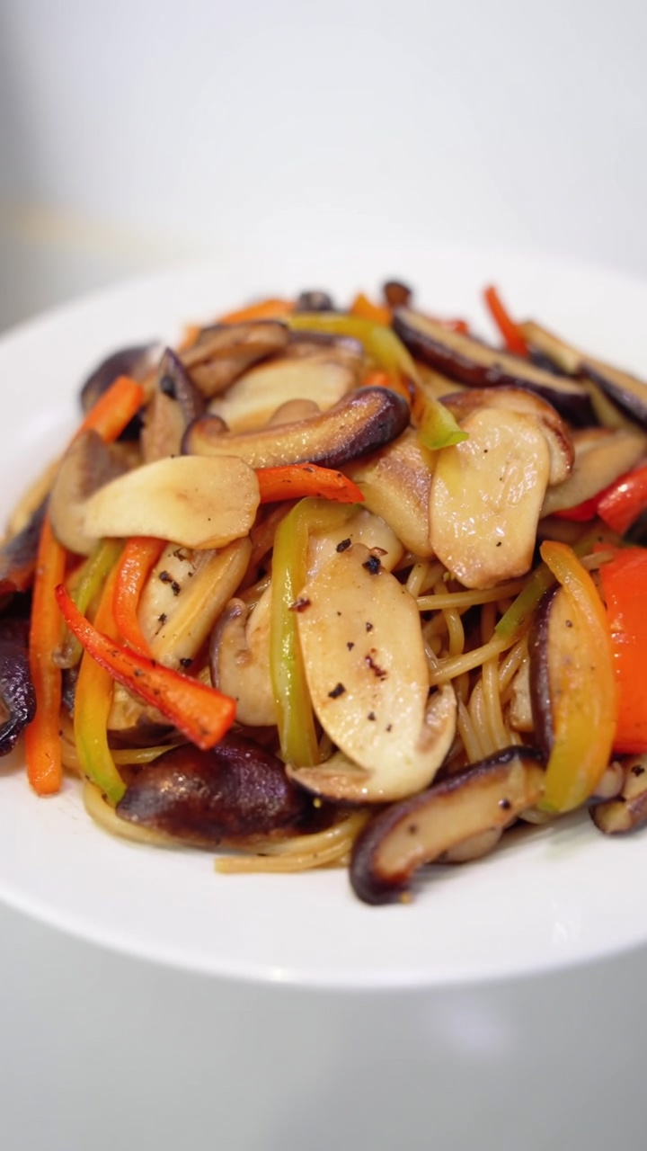 Apetyczna porcja spaghetti z podsmażonymi grzybami shiitake i sosnowymi, pociętą w paski kolorową papryką oraz obficie posypana świeżo mielonym pieprzem.
