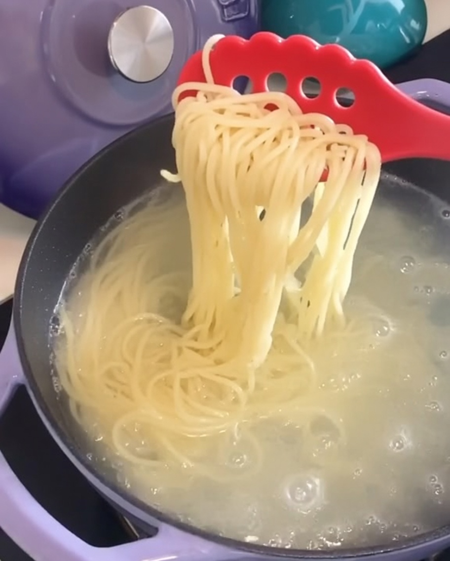Ugotowane spaghetti wyjmowane z garnka za pomocą widelca do makaronu.