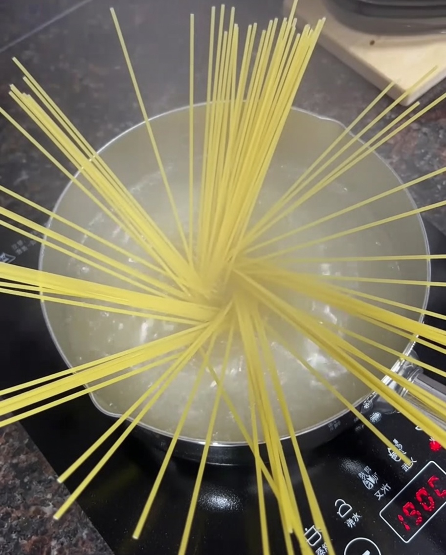 Surowe nitki spaghetti w garnku z wrzącą wodą.
