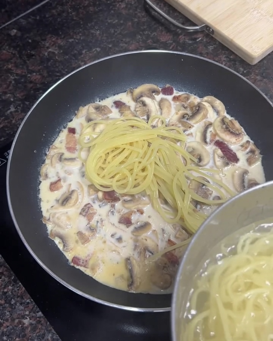 Gotowane spaghetti przenoszone z garnka na patelnię z sosem.