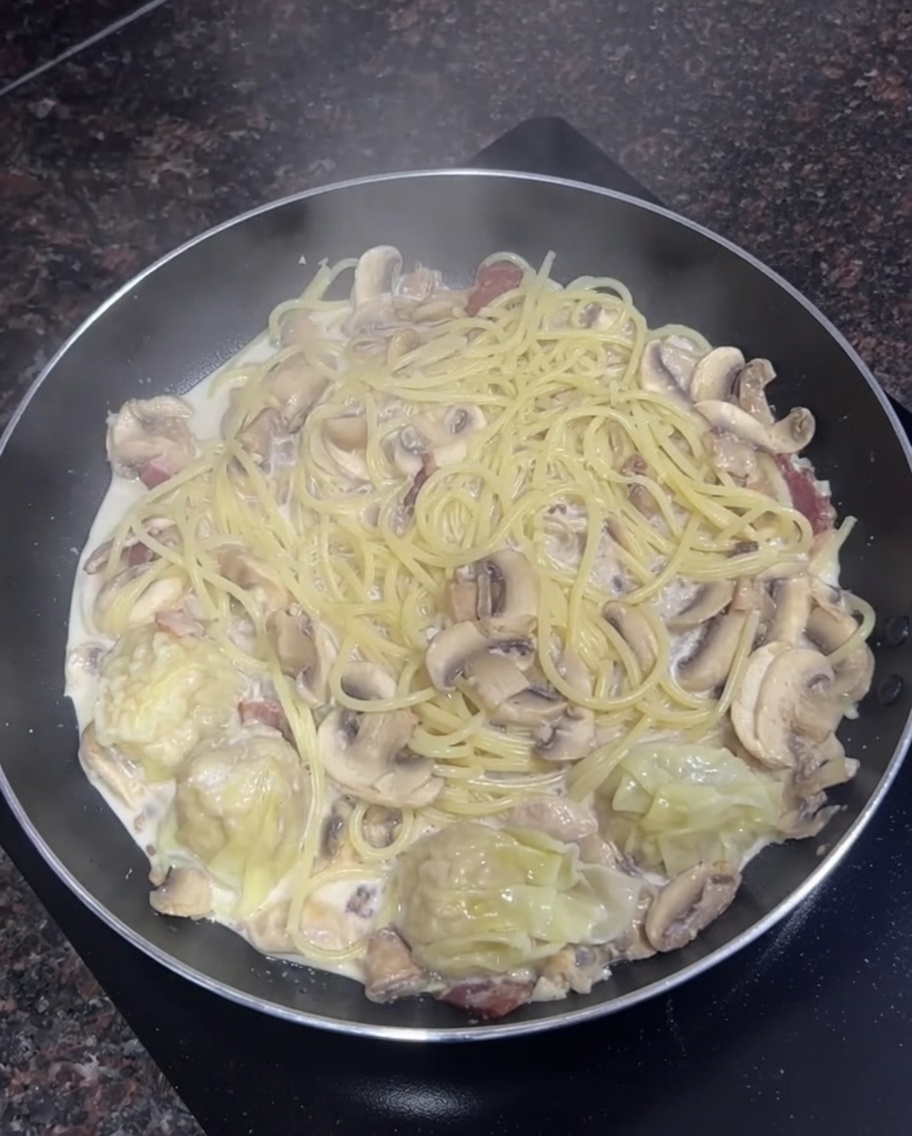 Patelnia z kremowym makaronem, pieczarkami i ugotowanymi wontonami.