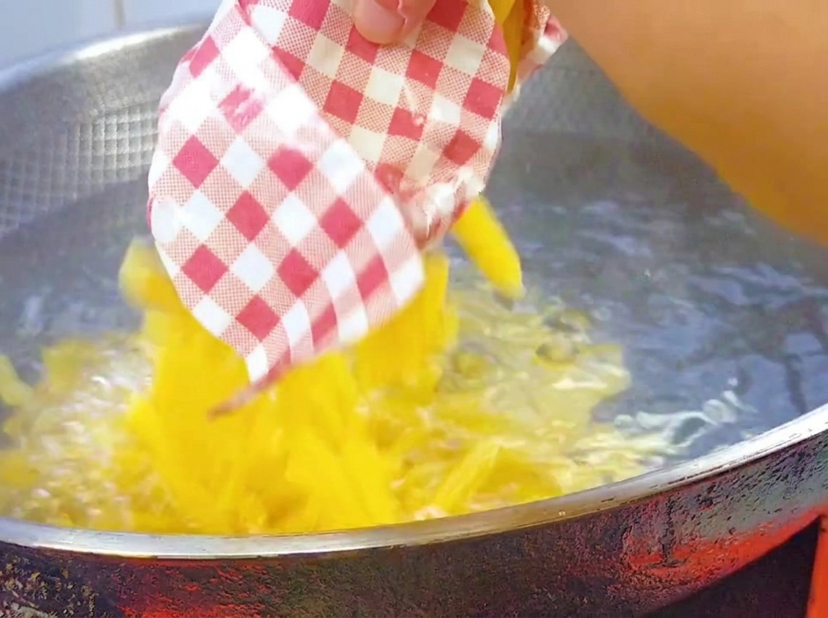Surowy makaron penne wsypywany do dużego woka z wrzącą, osoloną wodą.