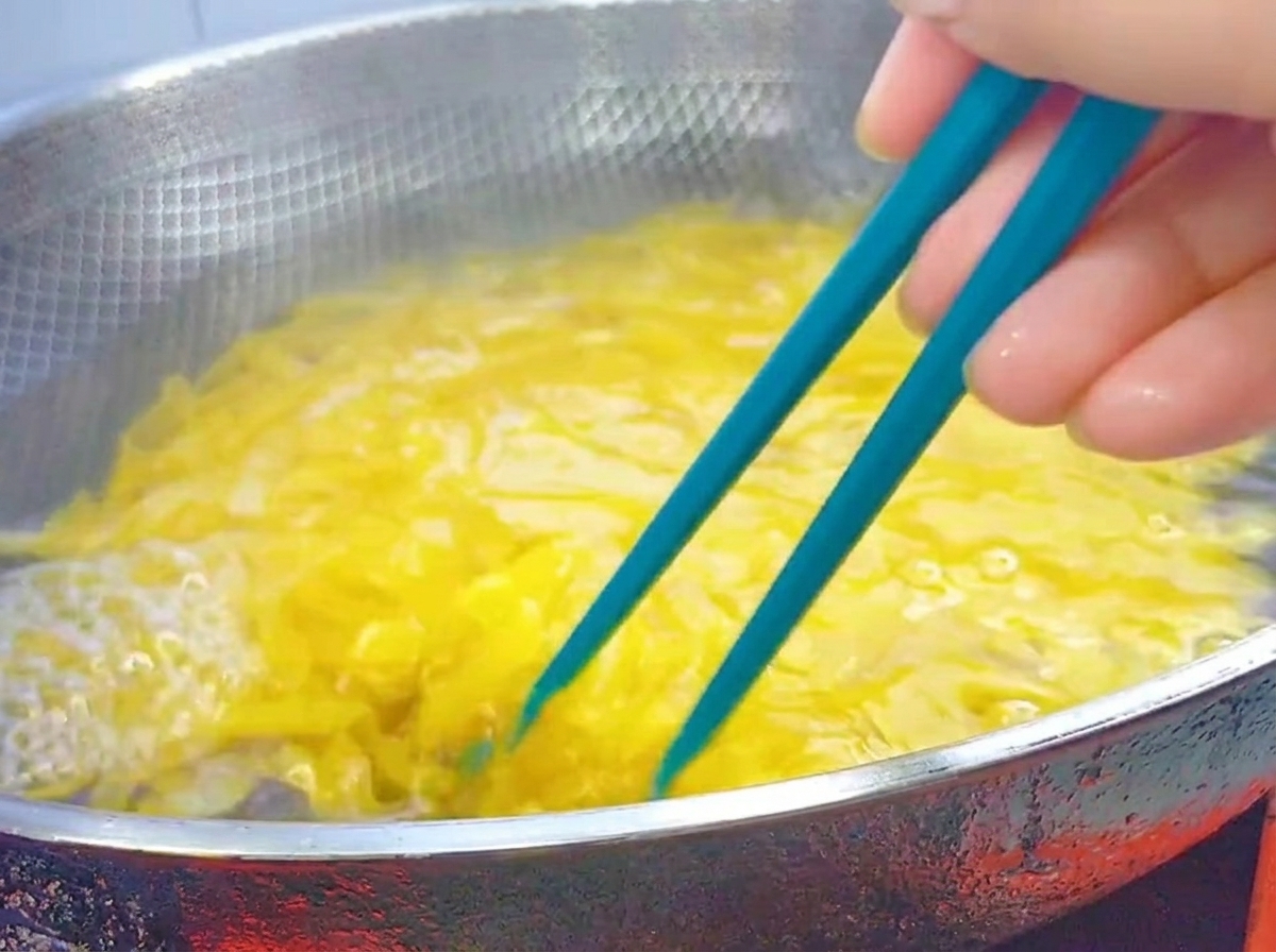 Niebieskie pałeczki mieszające gotujący się makaron penne w dużym woku ze stali nierdzewnej.