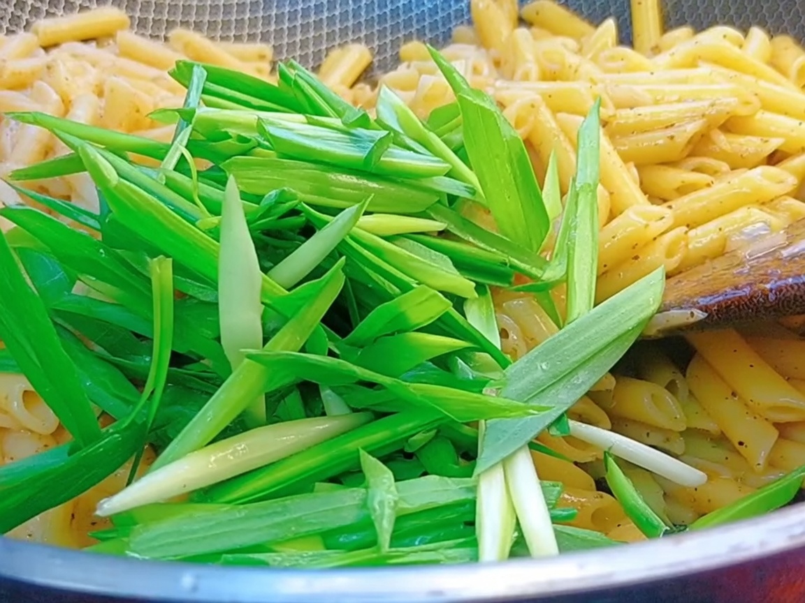 Świeże zielone pędy czosnku wrzucane do woka z makaronem penne w sosie pieprzowym.