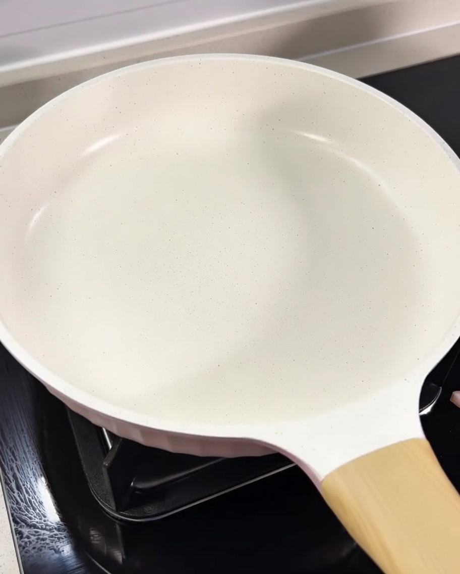 Pokrojone w kostkę guanciale rumieniące się na białej patelni we własnym wytopionym tłuszczu.
