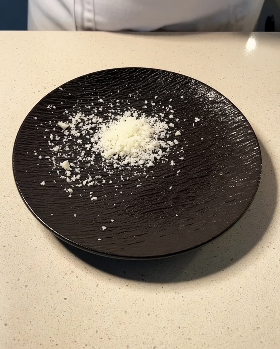 Świeżo starty parmezan i pecorino usypane na ciemnym, teksturowanym talerzu.