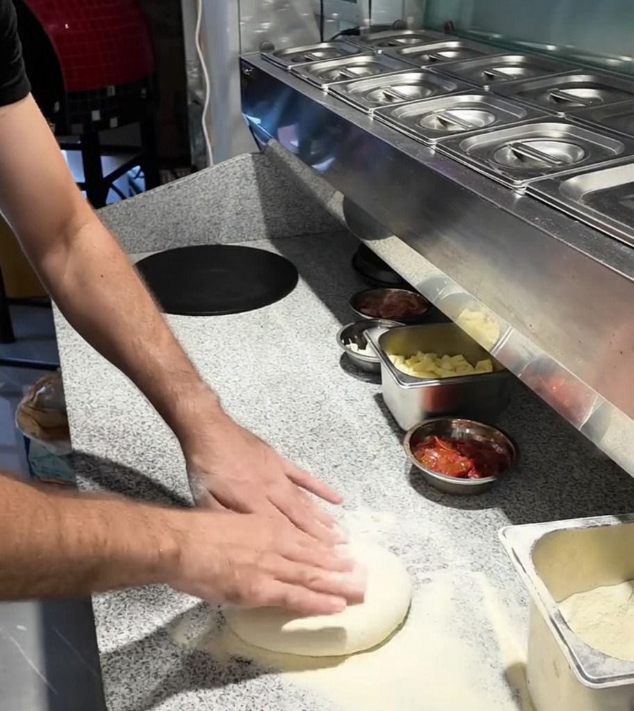 Ręce rozciągające kulkę ciasta na pizzę na blacie posypanym mąką.