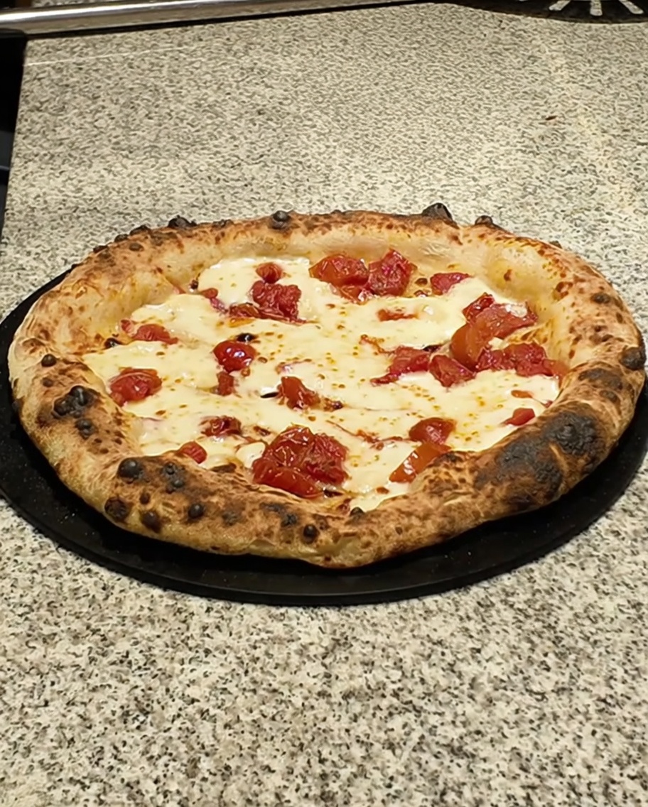 Gotowa pizza na ciemnym blacie, dekorowana plastrami pancetty.
